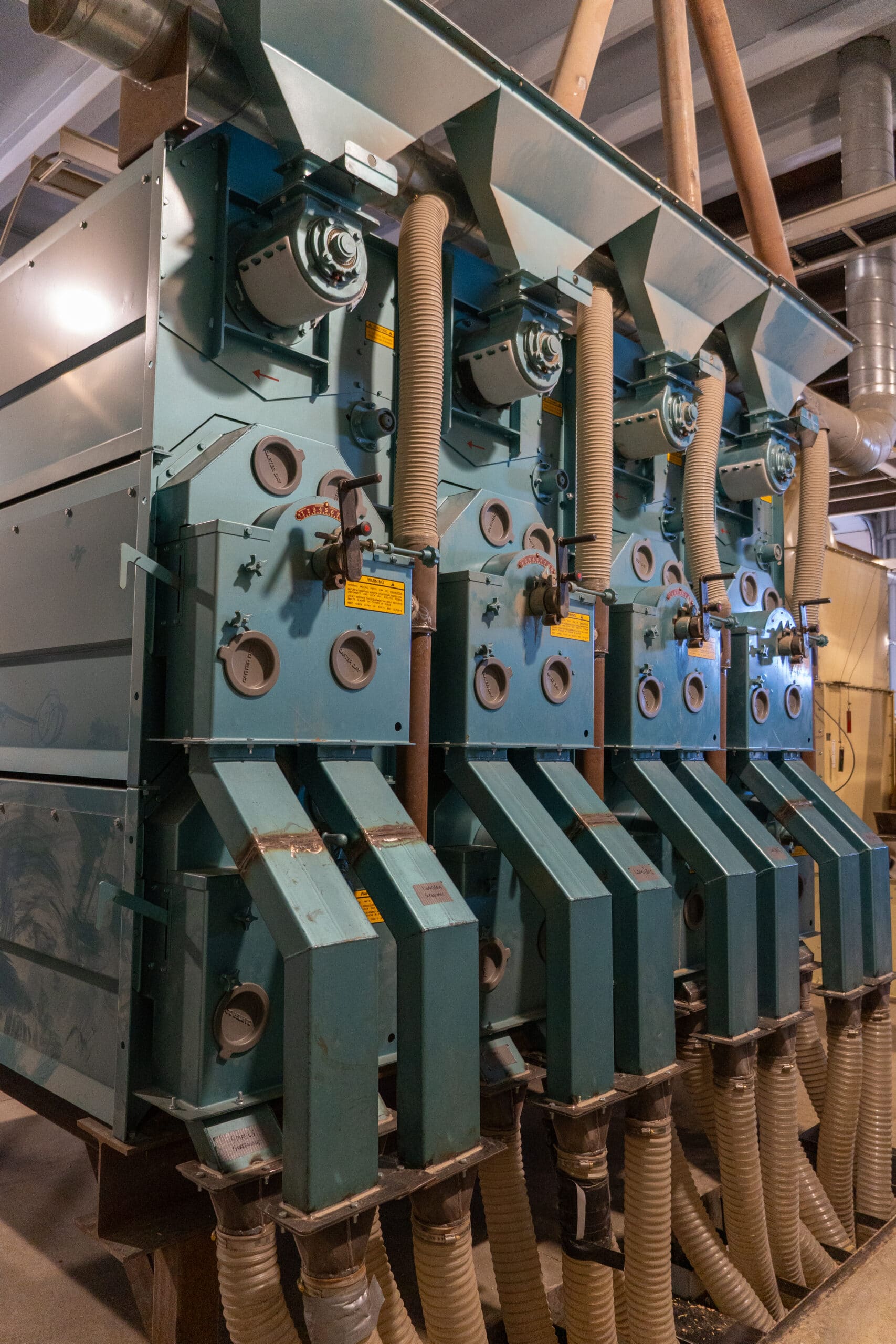 Row of Carter Day Uniflow indent separator stacks installed in a seed and grain processing plant with overhead spouting